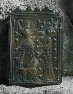 The storm-god Teisheba standing on his animal-attribute the lion, in front of him a worshipper. Votive plate from the kingdom of Urartu, Turkey. The upper od the plate has merlons like contemporary fortress walls. Bronze, H: 13,8 cm AO 28086